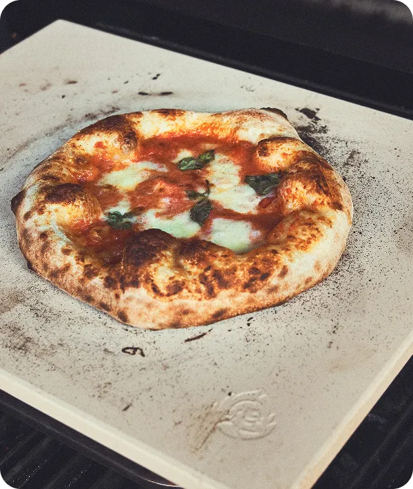 Pizza mit geschmolzenem Käse und luftiger Kruste auf Pizzastein im Gasgrill gebacken