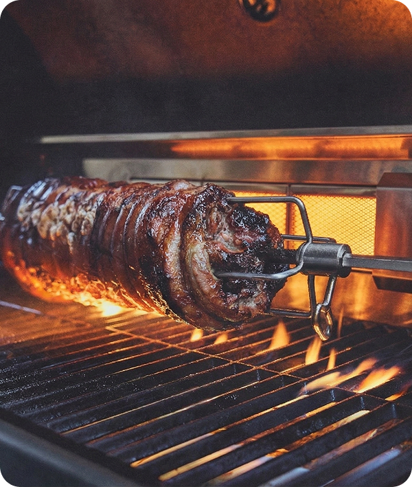Fleischspieß auf Drehspieß über offener Flamme im Gasgrill gleichmäßig gegrillt