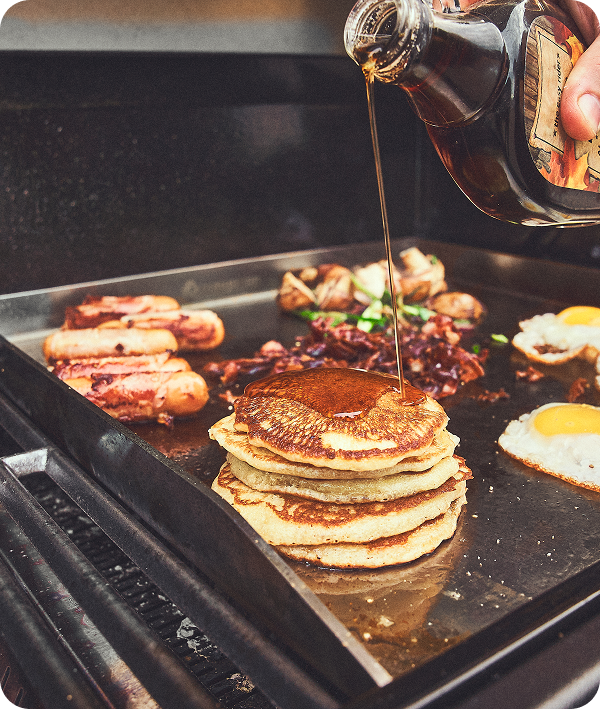 Pancakes, Spiegelei und Fleisch auf Plancha im Gasgrill mit Sirup beträufelt