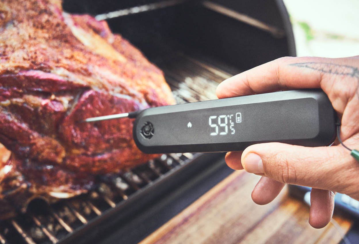 Fleisch-Garstufen: Einstich-Thermometer wird in Fleisch auf Gasgrill gestochen und zeigt Kerntemperatur an